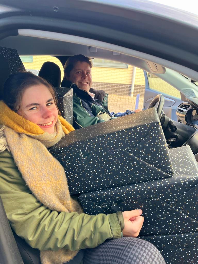Twee collega's onderweg in de auto met ingepakte cadeaus op schoot