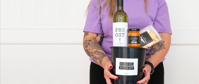 Iemand houdt een ingepakt cadeaupakket met fles en zoetigheid in de handen